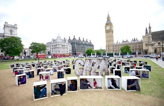 محتجون يجلسون في صناديق خشبية صغيرة تحاكي الظروف المعيشية في قطاع غزة الفلسطيني، أثناء وقفة احتجاجية تضامنية نظمتها منظمة أوكسفام الخيرية، لشرح معاناة سكان غزة، بالقرب من ساحة البرلمان البريطاني في العاصمة (لندن) - reuters  صورة وخبر - صحيفة الوسط البحرين